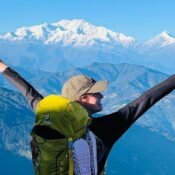 Hiker celebrating on mountain summit with trekking poles and panoramic snowy peaks