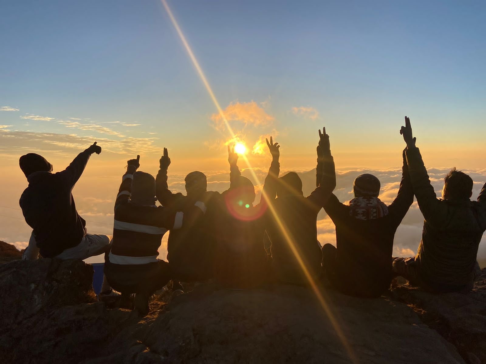 Group celebrating sunrise on mountain peak with peace signs.